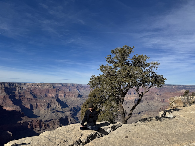 Shuo Ma sitting in front of the Grand Canyon.